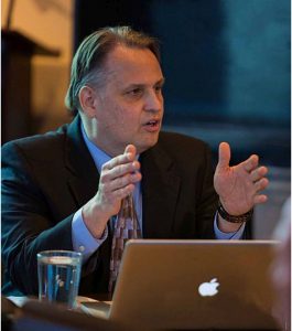 Martin Brossman sitting at a table talking with his hands.